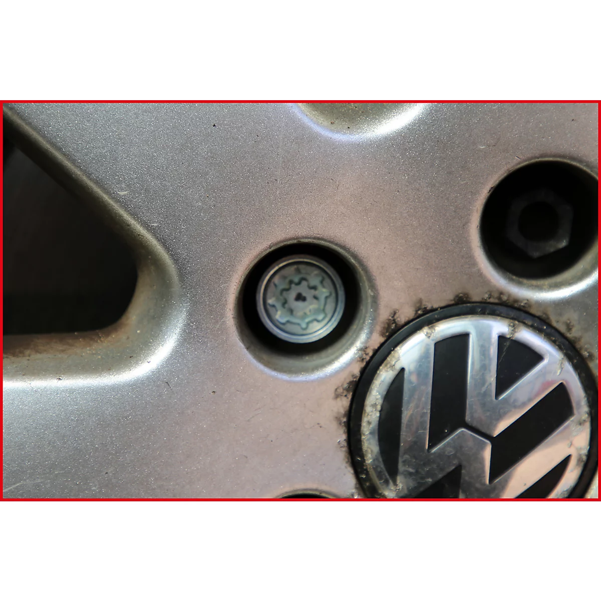 Nahaufnahme eines silbernen VW-Radkreuzes mit Radmuttern und VW-Logo.